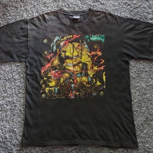 May include: A black short-sleeve t-shirt featuring a graphic print on the chest. The design displays a large yellow moon, dark swirling smoke, and red accents with the text "TWIZTID" in a stylized green font at the top right corner.