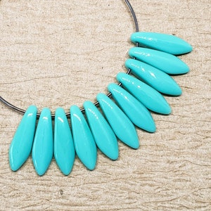 May include: A turquoise blue glass bead earring with a silver hoop. The beads are shaped like teardrops and are arranged in a fan shape.