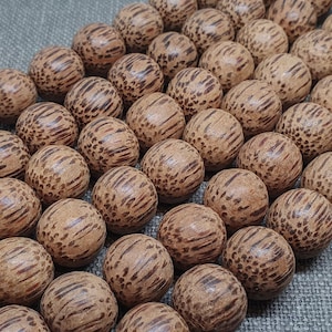 Puede incluir: Una hebra de cuentas de madera marrón con un patrón de veta de madera natural. Las cuentas son redondas y tienen un acabado liso y pulido.