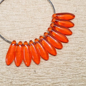 May include: Orange glass beads strung on a silver hoop earring. The beads are shaped like teardrops and are arranged in a fan shape.