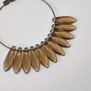 May include: A hoop earring with a silver metal hoop and a dangle of brown teardrop-shaped glass beads.