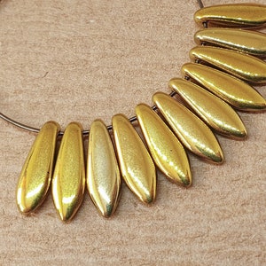 May include: A gold hoop earring with a row of gold teardrop-shaped beads hanging from the bottom. The beads are arranged in a fan shape.
