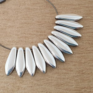 May include: Silver hoop earrings with a silver teardrop design. The earrings are made of metal and have a simple, elegant design.