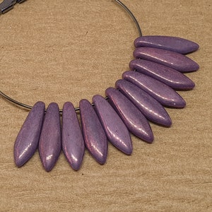 May include: A purple hoop earring with a silver hoop and purple wooden teardrop-shaped beads hanging from it.
