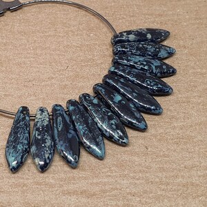 May include: A silver hoop earring with a row of dark blue and white ceramic teardrop-shaped beads.