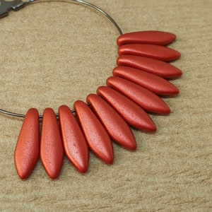 May include: A hoop earring with a silver metal hoop and a row of ten red, matte, teardrop-shaped beads.