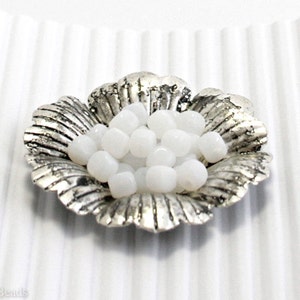 Può includere: Una piccola ciotola d'argento piena di perline rotonde opache bianche.