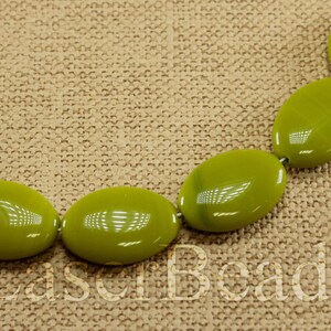 May include: A strand of oval-shaped green beads on a brown fabric background. The beads are smooth and glossy.