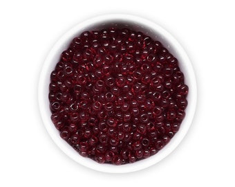 May include: A white bowl filled with small, round, red glass beads.