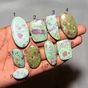 May include: Nine polished cabochon gemstones labelled 1 through 9, featuring a mix of light green and teal matrix with embedded vibrant pink and magenta mineral inclusions. The stones vary in oval, rectangular, and irregular shapes with smooth surfaces.
