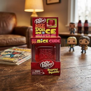 K&ouml;nnte beinhalten: Ein Dr Pepper Nee Doh Nice Cube Sensorik-Spielzeug in einer durchsichtigen Kunststoff-Verpackung. Die Verpackung zeigt das Dr Pepper Logo, den Text Nee Doh Nice Cube und den Schriftzug Suptid Squish. Das Spielzeug ist ein roter, transparenter W&uuml;rfel.