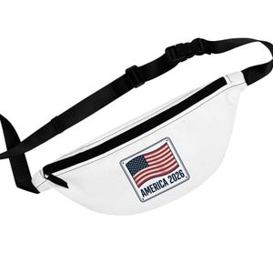 Può includere: Marsupio bianco con cinturino e fibbia neri regolabili. Il marsupio presenta una toppa rettangolare con la bandiera americana e la scritta "AMERICA 2026" in un bordo blu. Progettato per trasportare l'essenziale.