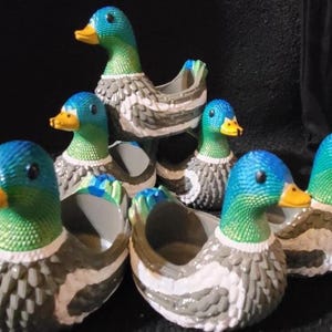 May include: A collection of ceramic duck planters. The ducks have blue and green heads with yellow beaks, gray and white bodies, and are arranged in a group. The planters are suitable for small plants or decorative use.