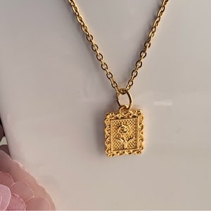 May include: Gold-toned necklace featuring a rectangular pendant with a rose design. The pendant is framed with an ornate border. The chain is delicate and the necklace is displayed against a white background.