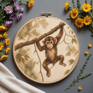 May include: A circular wooden embroidery hoop containing a cross-stitch pattern of a brown monkey hanging from a tree branch. The background of the stitch work features light beige fabric with green leaf silhouettes, creating a detailed nature scene.