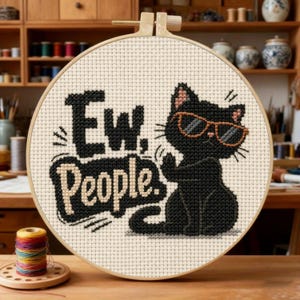 May include: A round wooden embroidery hoop containing a cross-stitch design on cream fabric. The design features a black cat wearing orange-rimmed sunglasses and the black text "Ew. People." The cat is positioned to the right of the text.