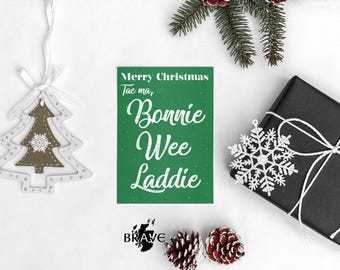 Può includere: Una scena natalizia festosa con una carta verde che recita "Merry Christmas Tae ma, Bonnie Wee Laddie" in scrittura bianca. Una scatola regalo nera con spago bianco, un ornamento a fiocco di neve e un ornamento per albero di Natale sono anche presenti.