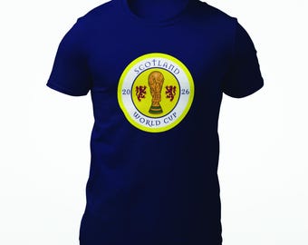 Puede incluir: Camiseta azul marino con un emblema circular. El emblema presenta el texto "SCOTLAND WORLD CUP", un trofeo y dos leones rojos sobre fondo amarillo. También están presentes los años "20" y "26".
