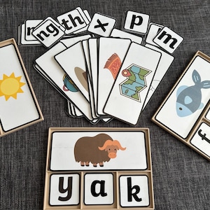 May include: A set of educational phonics cards featuring illustrations and letter tiles. The cards display images like a yellow sun, a blue fish, and a brown yak, alongside letter tiles spelling words like sun, fish, and yak. Includes various letter combinations like ng, th, x, p, and m.