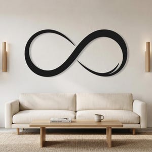 Pode incluir: Uma grande peça de arte de parede com o símbolo do infinito em preto montada numa parede lisa. O design apresenta uma forma de laço fluido e contínuo com um acabamento mate suave, posicionado horizontalmente acima de um sofá claro.