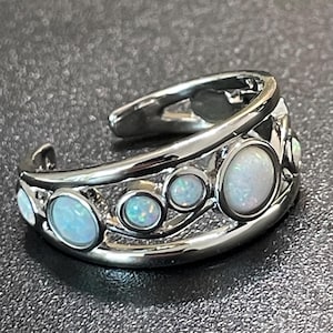 May include: A silver-toned open band ring featuring a series of five round, iridescent white opal-like stones of varying sizes set within a polished metal frame that curves along the finger with an open gap at the top.