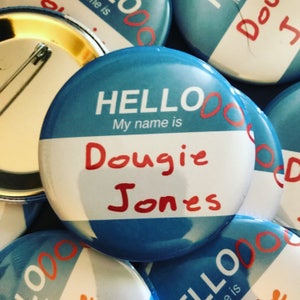 May include: Blue button with the text "HELLO My name is Dougie Jones" in red lettering. The button has a gold pin on the back.