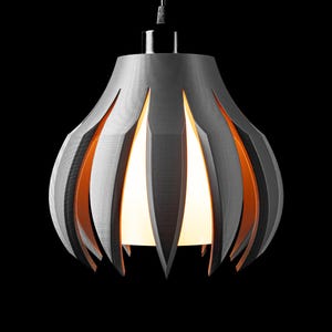 Op de afbeelding: Een moderne grijze hanglamp met een uniek, gelaagd ontwerp. De lamp heeft verticale uitsparingen die een oranje interieur en een heldere witte lichtbron onthullen. De armatuur hangt aan een dunne draad tegen een zwarte achtergrond.