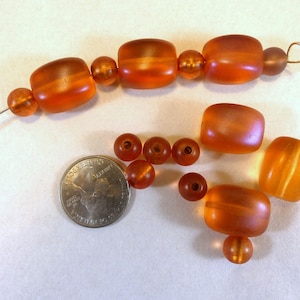 May include: A collection of amber glass beads in various shapes and sizes. The beads are strung on a wire and some are loose. The beads are a mix of orange and brown.