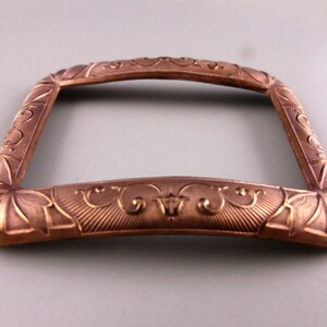 May include: A decorative, ornate, copper-colored metal frame with an intricate design. The frame has a rectangular shape with rounded corners and a slightly curved top.