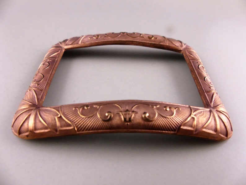 May include: A decorative, ornate, copper-colored metal frame with an intricate design. The frame has a rectangular shape with rounded corners and a slightly curved top.