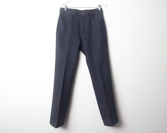 Può includere: Un paio di pantaloni grigi scuri appesi a un'appendiabiti bianca su uno sfondo bianco.
