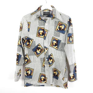 Pode incluir: Camisa abotoada com fundo cinza e um padrão repetido de imagens emolduradas. As molduras são azuis, amarelas e marrons, com um personagem de desenho animado dentro. Linhas brancas verticais também estão presentes.