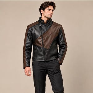 Puede incluir: Una chaqueta de bloques de color que combina paneles negros y marrones. La chaqueta tiene un cuello alto, una cremallera frontal completa y mangas largas. El diseño incorpora líneas diagonales en el pecho, creando un patrón geométrico con texturas contrastantes similares al cuero.