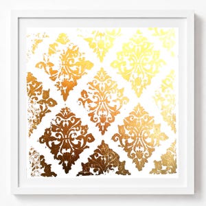 Può includere: Un'opera d'arte da parete quadrata con sfondo bianco e un motivo damascato ripetuto in foglia d'oro. Il design in oro metallizzato è composto da motivi floreali ornamentati a forma di diamante con una finitura testurizzata e usurata, racchiusa in una cornice bianca.