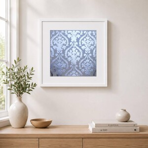 Può includere: Un'opera d'arte murale quadrata in una cornice bianca con un motivo damascato ripetuto in tonalità azzurro e argento. L'opera mostra intricati motivi floreali e a volute simmetrici stampati su uno sfondo a tinta unita, montata su una parete.