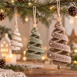May include: Three spiral-shaped Christmas tree ornaments made of crocheted yarn in cream, sage green, and taupe. Each ornament features a wooden star at the top, a hanging loop, and small gold jingle bells and white beads attached along the spiral.
