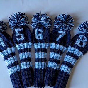May include: Set of six blue and white striped golf club head covers with pom poms. Each cover has a number from 4 to 9 knitted on the front.