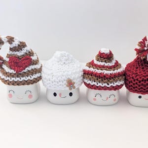 Puede incluir: Cuatro tazas de cer&aacute;mica blanca con diferentes gorros de punto. Los gorros son de rayas marrones y blancas, blancos, de rayas marrones y rojas y rojos. Cada taza tiene una cara sonriente.