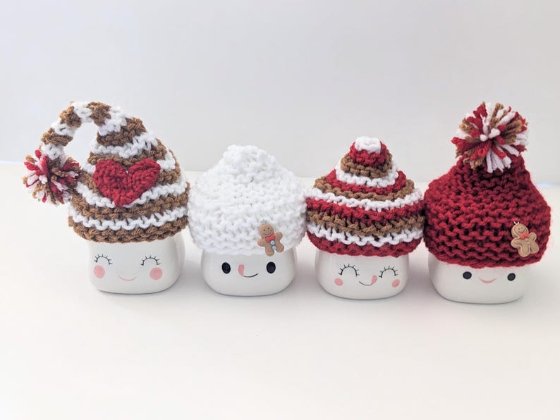 Puede incluir: Cuatro tazas de cer&aacute;mica blanca con diferentes gorros de punto. Los gorros son de rayas marrones y blancas, blancos, de rayas marrones y rojas y rojos. Cada taza tiene una cara sonriente.