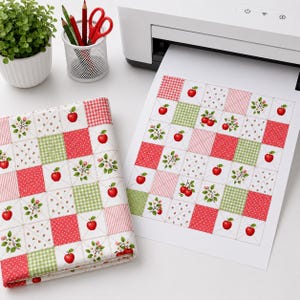 Puede incluir: Un cuadrado de tela doblado y una hoja de papel impresa, ambos con un patr&oacute;n de patchwork repetitivo de manzanas rojas, cuadros vichy verdes y motivos florales. El dise&ntilde;o consiste en cuadrados alternos en rojo, verde y blanco con manzanas.