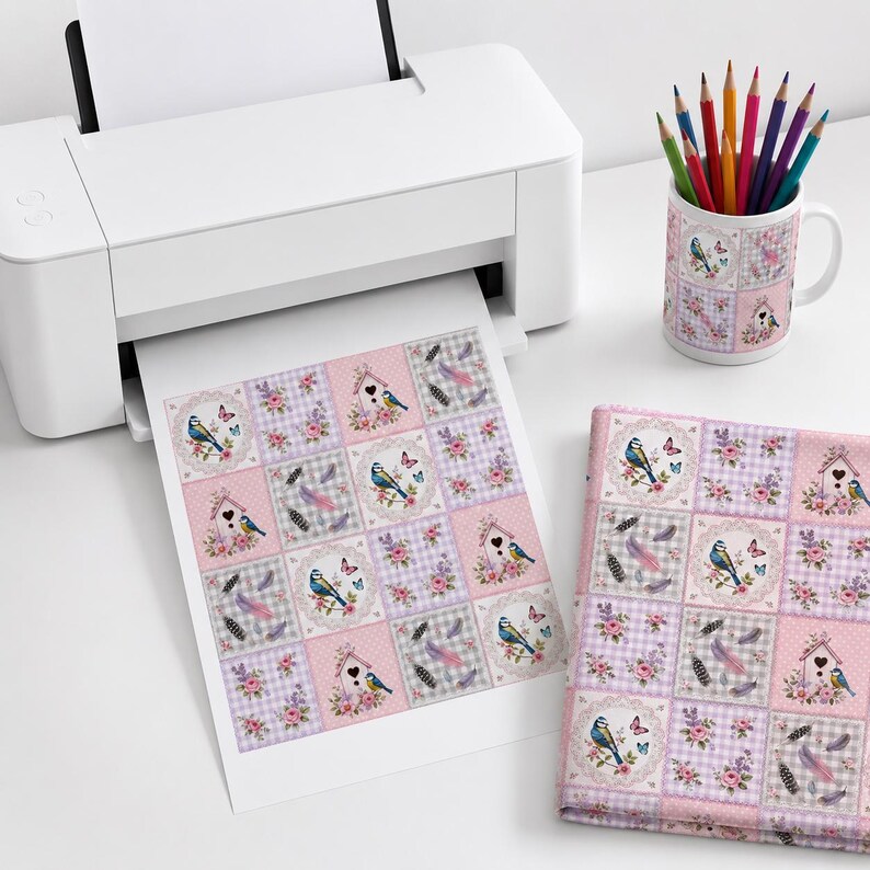 Peut inclure: Une imprimante blanche &eacute;mettant une feuille de papier avec un motif en grille repr&eacute;sentant des oiseaux bleus, des nichoirs, des roses roses et des plumes. Un mug en c&eacute;ramique assorti rempli de crayons de couleur et un tissu pli&eacute; affichent le m&ecirc;me motif.
