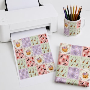 Op de afbeelding: Een witte printer voert een vel papier uit met een herhalend rasterpatroon van pompoenen, heksenbezems, vleermuizen en aardbeien. Een bijpassende keramische mok gevuld met kleurpotloden staat ernaast, samen met een gevouwen vierkant van stof.
