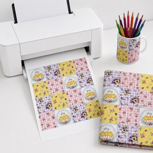 May include: A white printer outputting a sheet of paper with a grid pattern of yellow chicks, floral motifs, and pink and purple gingham squares. A matching ceramic mug holds a collection of coloured pencils, and a folded fabric swatch sits nearby.