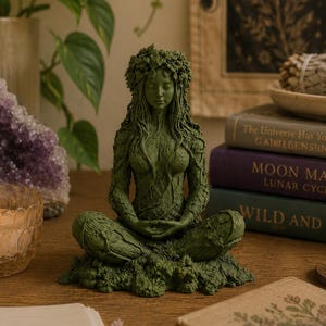 Pode incluir: Uma escultura verde-escura de uma figura em pose meditativa, com uma coroa de folhas e um corpo texturizado com padrões intrincados de vinhas e ramos. A figura está sentada de pernas cruzadas sobre uma base de folhagem com olhos fechados.