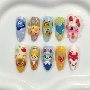 May include: A set of ten almond-shaped acrylic nails, each uniquely decorated with colorful, cartoon-style designs. The designs include characters, patterns, and 3D elements in various colors, including blue, yellow, pink, and green.
