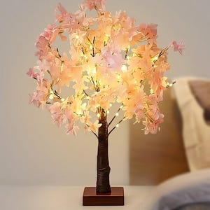May include: A decorative cherry blossom tree lamp with soft pink flowers and warm white LED lights. The tree has a brown trunk and sits on a dark brown rectangular base. The lamp is designed for indoor use.