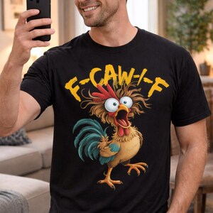 May include: A black short-sleeved t-shirt featuring a graphic of a wide-eyed, disheveled rooster with brown and blue feathers. Above the rooster, the yellow text reads F-CAW-F. The design is centered on the chest of the garment.