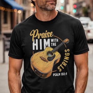 May include: Black t-shirt featuring a detailed illustration of an acoustic guitar. The shirt includes the text "Praise Him with the Strings" in a gold and white design, with "Psalm 150:4" below the guitar.