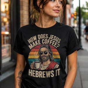 Puede incluir: Camiseta negra con el texto "HOW DOES JESUS MAKE COFFEE? HEBREWS IT" y un gráfico de Jesús con gafas de sol, sosteniendo una taza de café. El diseño incluye un atardecer retro.