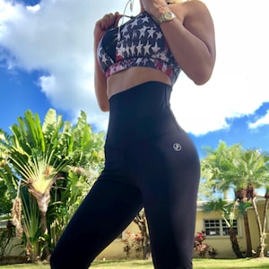 May include: A sports bra featuring a red, white, and blue star-patterned design paired with solid black high-waisted leggings. The leggings include a small circular logo on the left hip. The outfit is designed for athletic activity and movement.